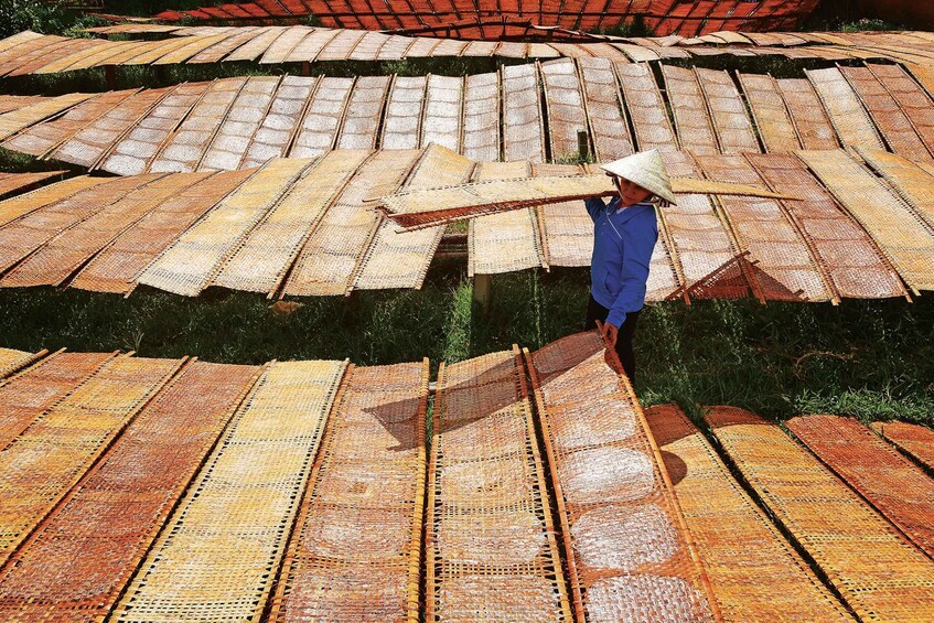 A person carrying a long, flat object across a field of large, rectangular mats. 1
