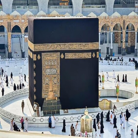 The Kaaba in the center of the Masjid al-Haram, surrounded by a large courtyard with people walking around. 1