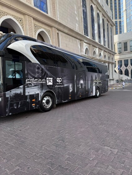 A tour bus parked in front of a large building with arched windows and a tiled facade. 4