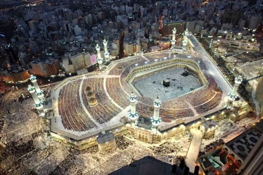 A large, illuminated mosque complex with a central courtyard, minarets, and surrounding urban area. 5