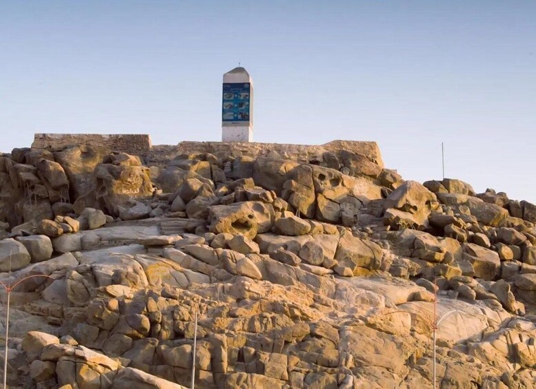 A rocky landscape with a tall monument featuring a blue informational panel. 3