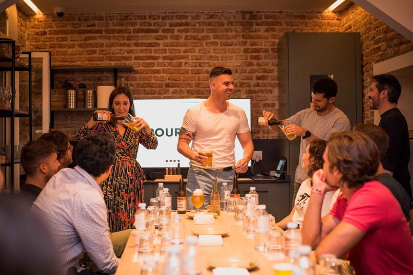 A group of people in a room with a brick wall, a presentation screen, and a table with bottles and glasses. 3