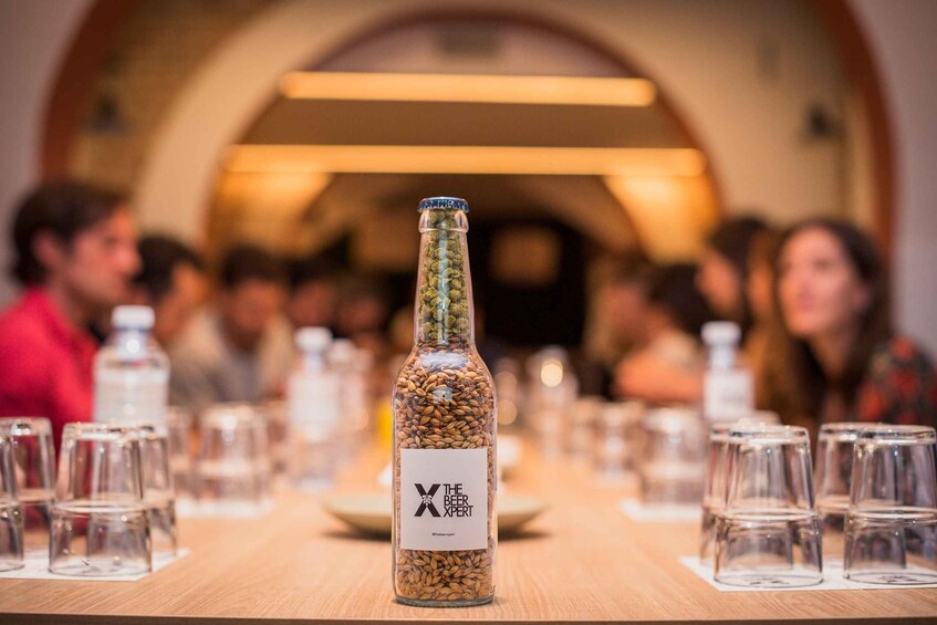 A bottle of beer with a label in the center of a table surrounded by empty glasses. 1