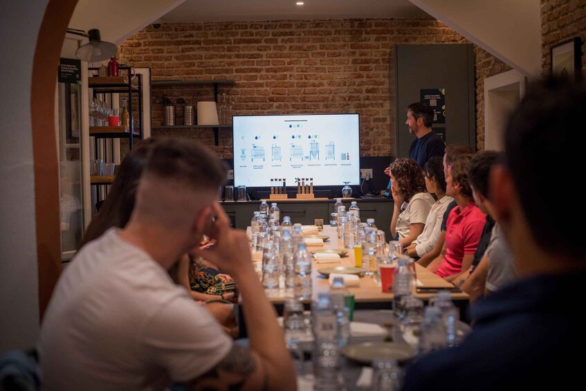 A group of people seated at a table with a presentation screen in a brick-walled room. 2