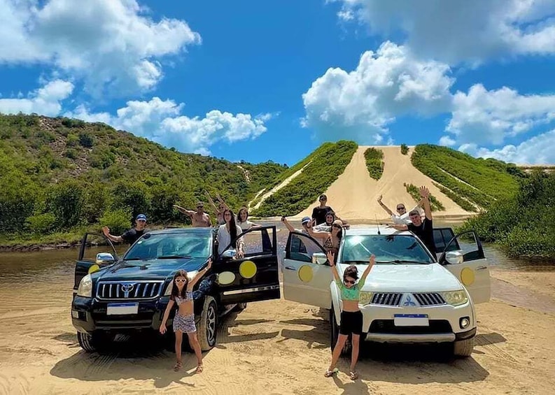 Two cars parked on a sandy beach with people standing around them. 1