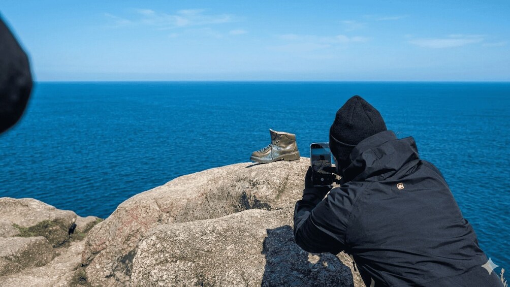 A person taking a photo of a pair of boots on a rock by the sea. 3