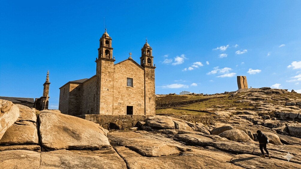 A historic stone church with two bell towers, set against a clear blue sky, surrounded by large rocks and a hilly landscape. 2