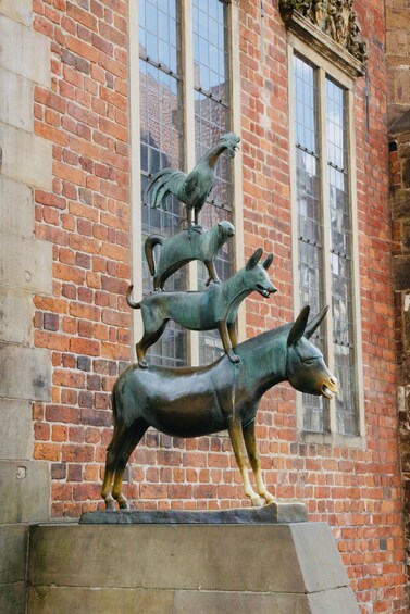 A bronze sculpture of three animals on a pedestal in front of a brick building with large windows. 3