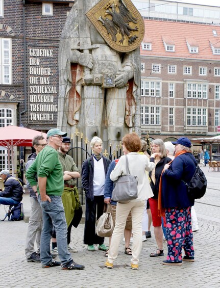 A group of people standing in front of a historical monument with inscriptions and a coat of arms. 2
