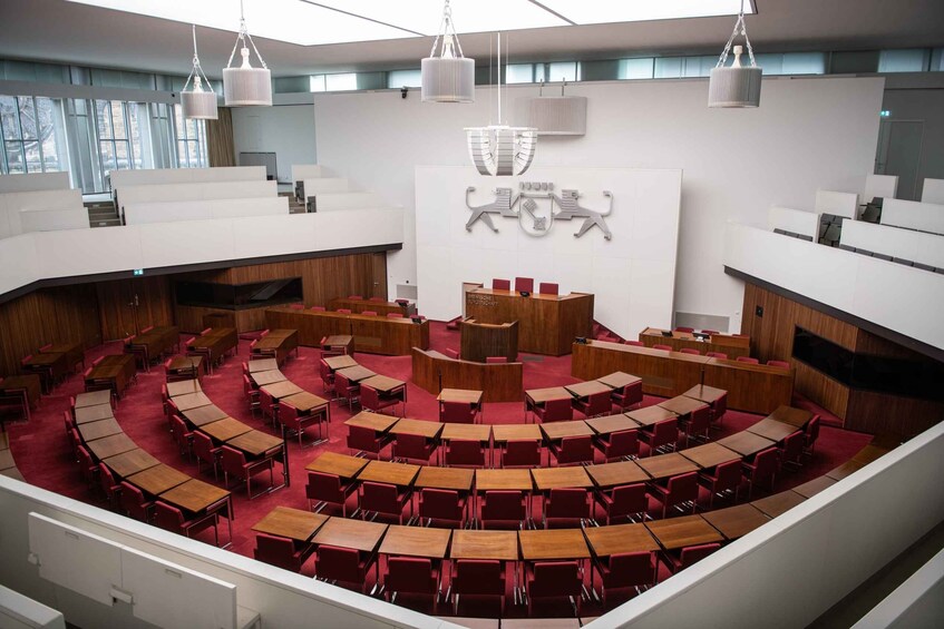 A modern conference room with tiered seating, wooden tables, and red chairs. 1