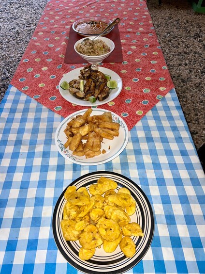 A table with a red polka dot tablecloth and a blue and white checkered tablecloth. On the table, there are three plates: one with fried rice, one with fried plantains, and one with grilled meat. 5