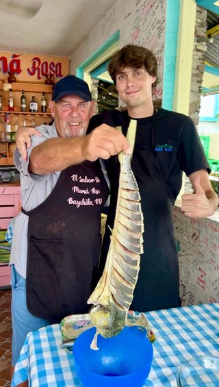 Two people holding a large fish, with a table and a blue bowl in front. 4