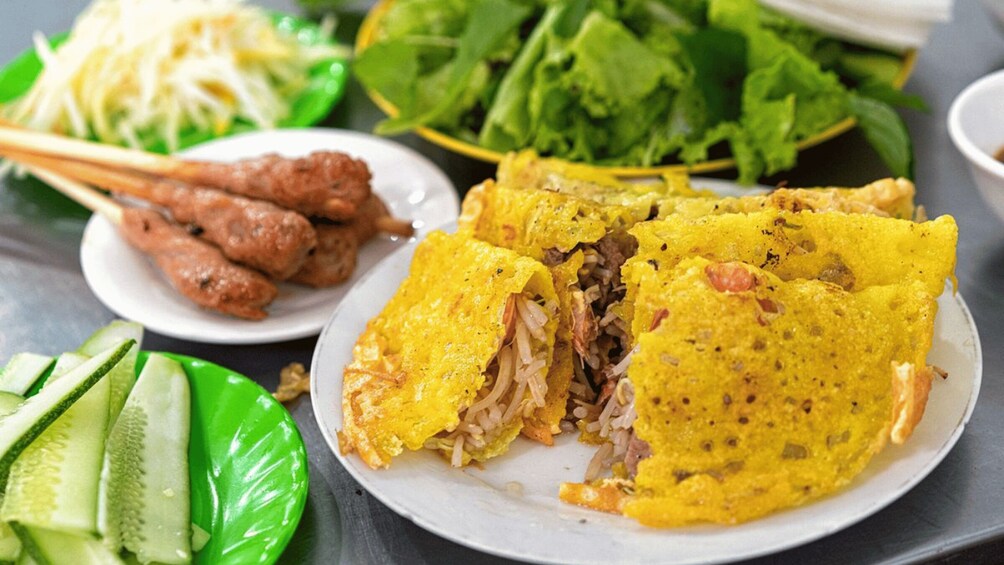 A plate of yellow crepes filled with meat and vegetables, accompanied by cucumber slices, a salad, and a plate of fried chicken. 5