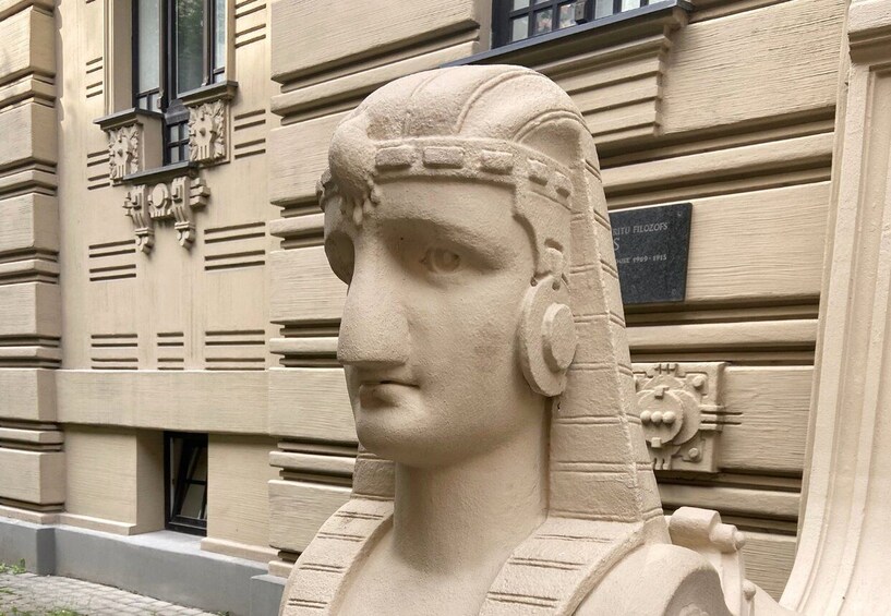 A stone bust sculpture on a building facade with decorative moldings and a plaque. 2