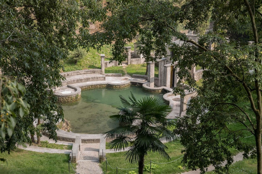 A circular water feature with stone steps and columns, surrounded by lush greenery and trees. 5