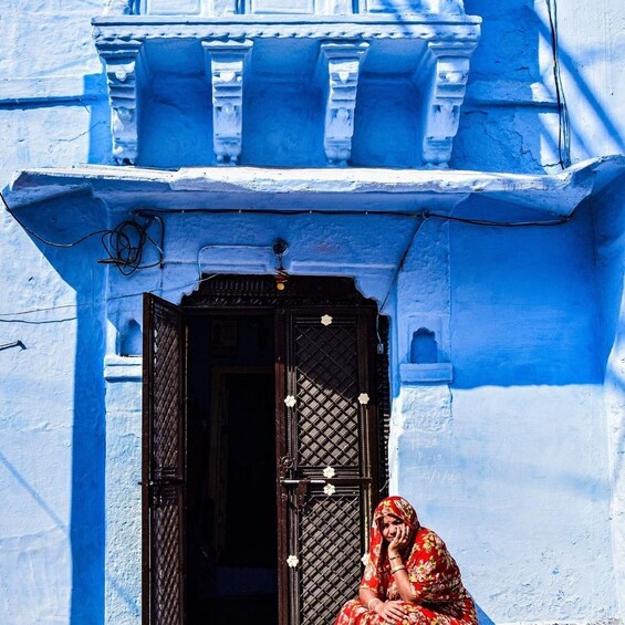 A woman sitting in front of a blue-painted building with a black door. 3