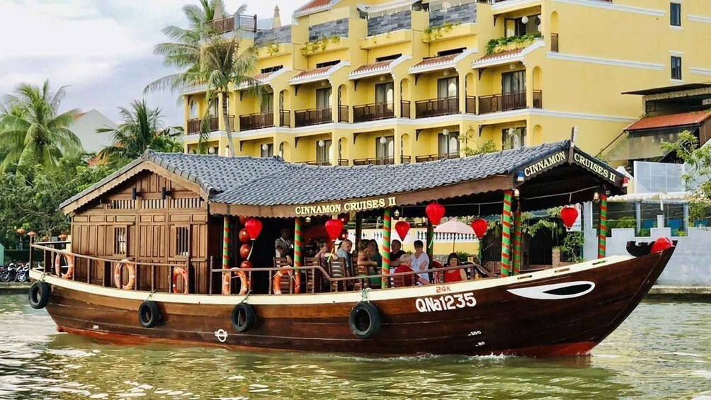 A traditional wooden boat with 'CINNAMON CRUISES II' written on its side, floating on water with a yellow building in the background. 3