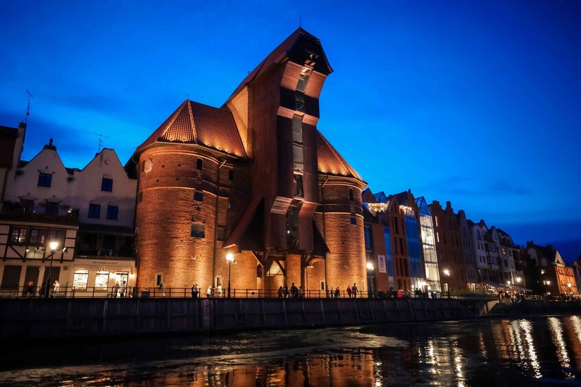 A historic building with a prominent tower and brick walls, located by a river with reflections. 2