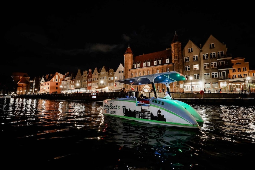 A city boat with a green and white design, docked at a waterfront with illuminated buildings in the background. 4