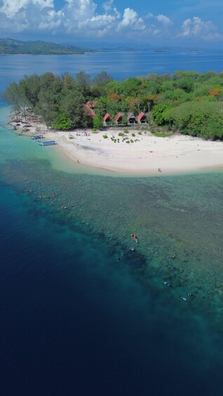 An aerial view of a beach with clear turquoise waters, a sandy shore, and several red-roofed structures. 1