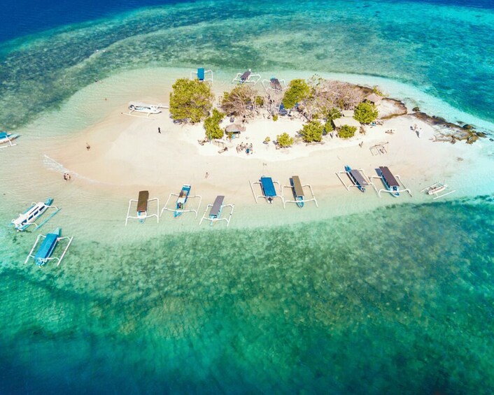 An aerial view of a tropical island with clear turquoise waters, a sandy beach, and several blue lounge chairs. 4