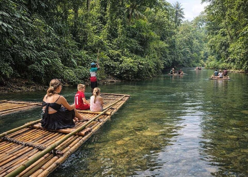 People on a bamboo raft in a river surrounded by dense forest. 1