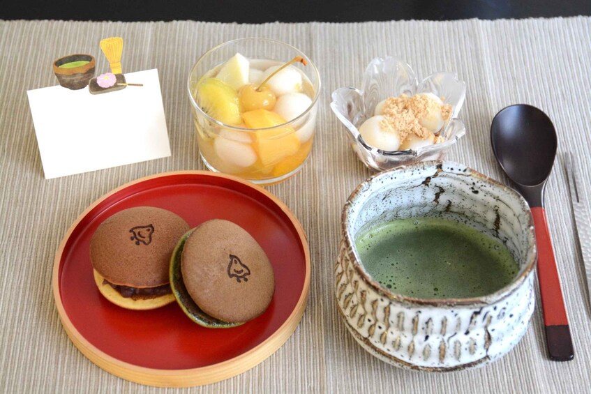 A traditional Japanese meal with mochi, a green tea cup, and a bowl of fruit. 1