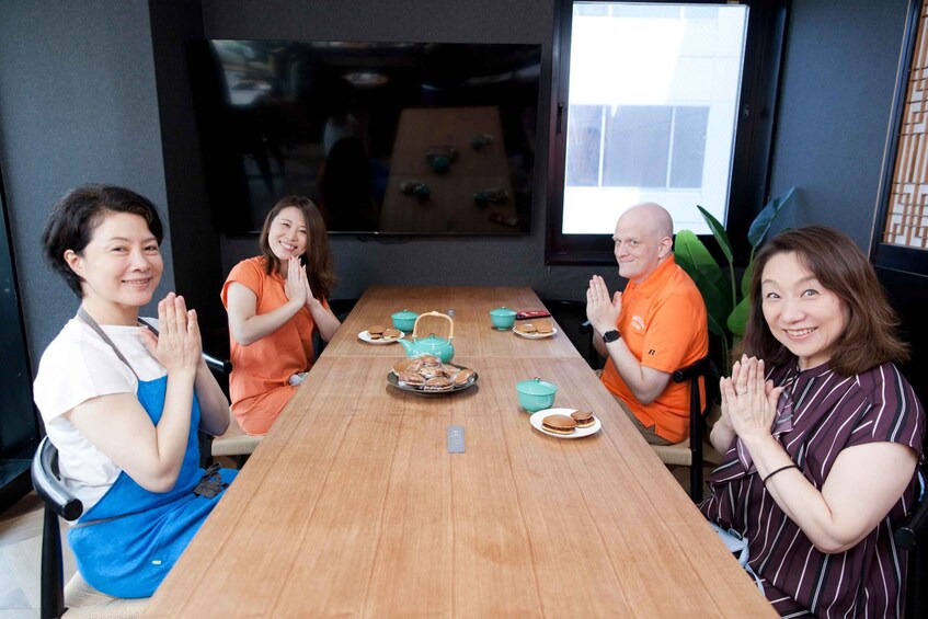 Four people seated around a wooden table with a teapot, cups, and plates of food. 5