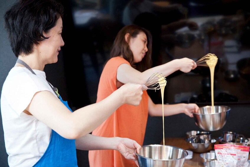 Two people cooking, one whisking batter and the other holding a bowl. 4