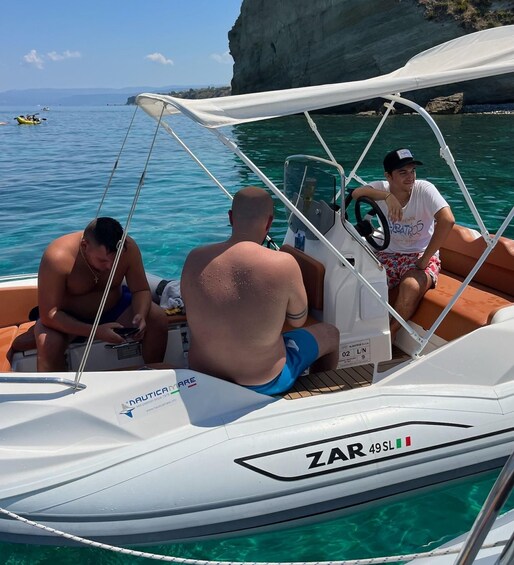 A boat with three people, clear turquoise water, and rocky cliffs in the background. 2