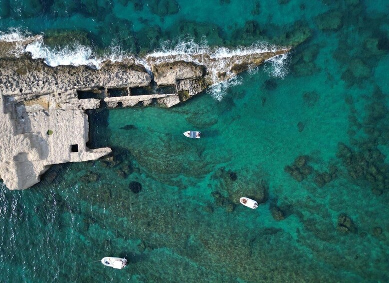 A coastal area with clear turquoise waters, rocky cliffs, and several boats anchored near the shore. 3