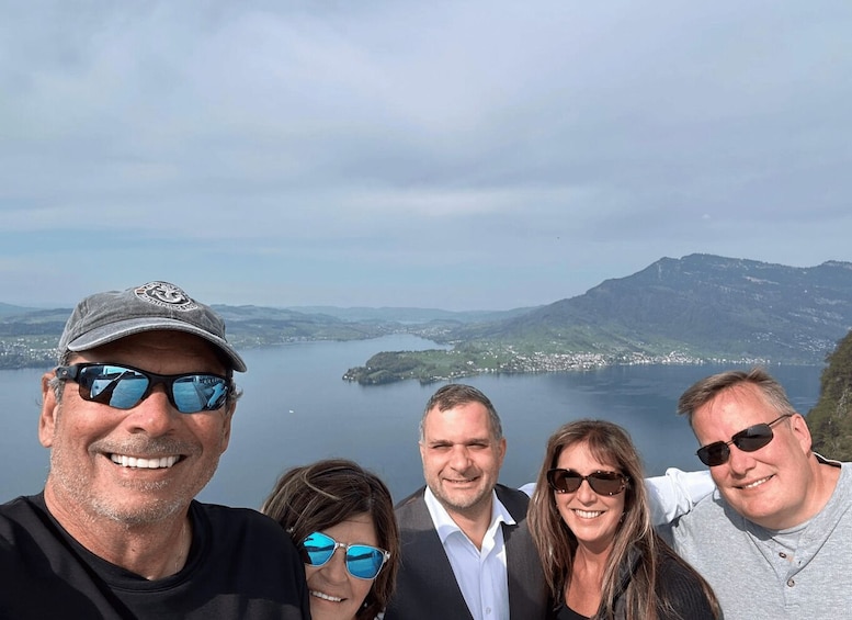 A group of people at a scenic overlook with a lake and mountains in the background. 4