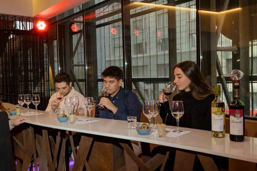 Three people tasting wine at a bar with a modern interior. 3
