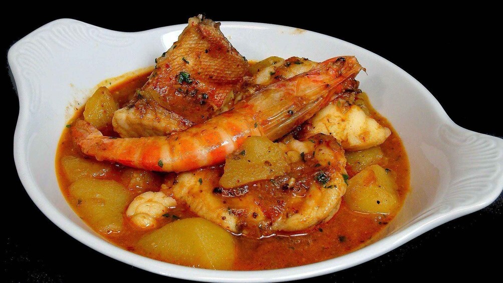 A dish of seafood with shrimp and potatoes in a red sauce. 5