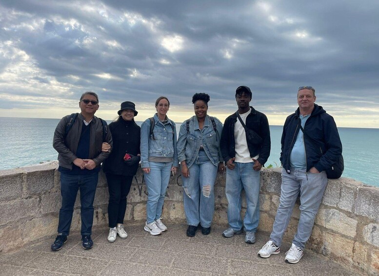 A group of people standing by a stone wall overlooking the sea under a cloudy sky. 2