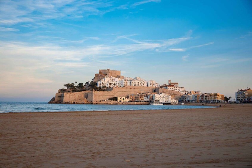 A coastal city with a prominent castle on a hill, a beach in the foreground, and a clear sky. 1