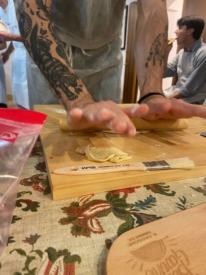 A person rolling dough on a wooden board with a floral tablecloth. 5