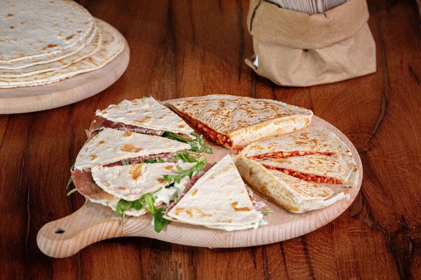 A wooden cutting board with a quesadilla cut into triangles, a stack of tortillas, and a cloth bag in the background. 3