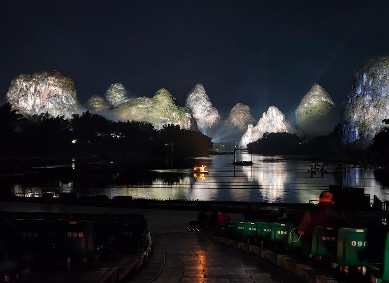 A nighttime view of a lake with illuminated rock formations and a dock with boats. 5