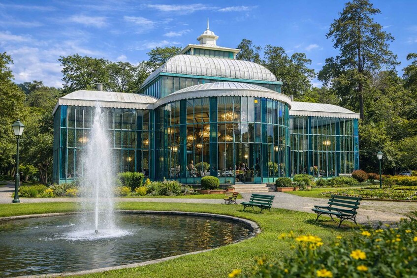A conservatory with a fountain, surrounded by a well-maintained garden and benches. 2