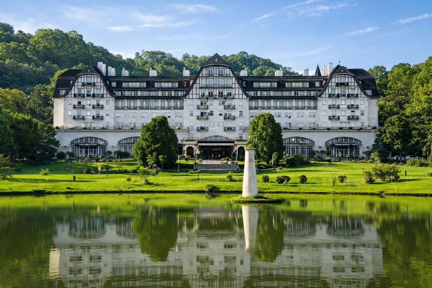 A large, white, multi-story building with a symmetrical facade, surrounded by a well-manicured lawn and a reflective pond. 1