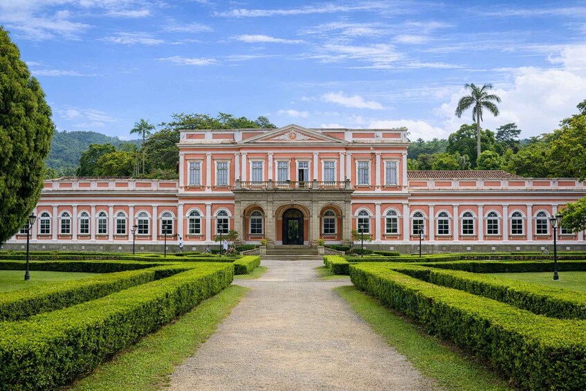 A large pink building with a central entrance, surrounded by manicured hedges and a clear sky. 5