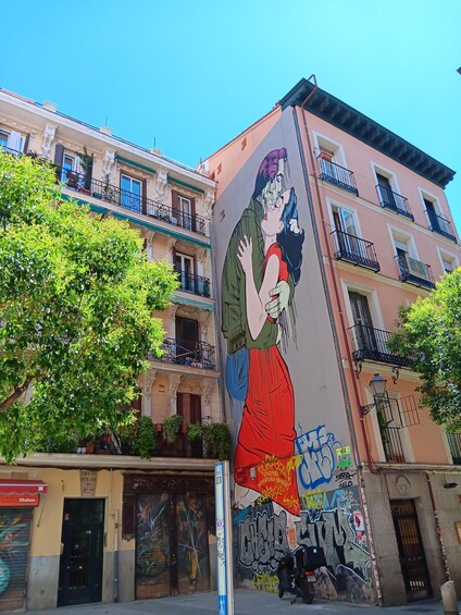 A mural of a couple on a building, with balconies and trees around. 1