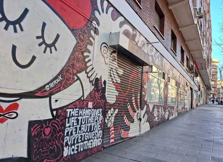 A mural with a hand giving life to a puppet on a building wall. 5
