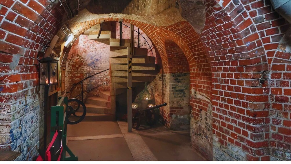 An arched brick passageway with a spiral staircase leading to a higher level. 1