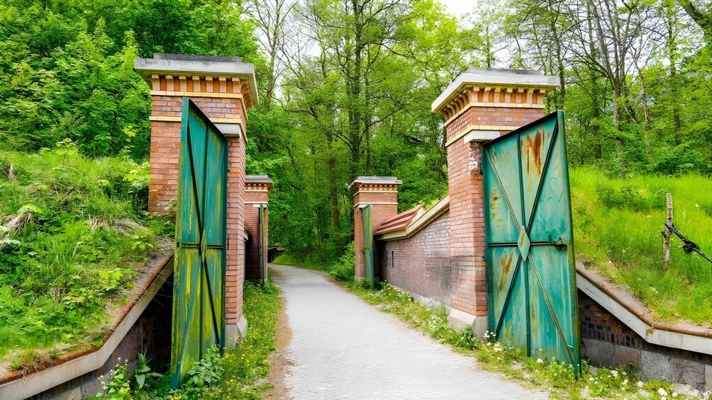 A pathway flanked by brick walls and green gates, surrounded by lush greenery. 2