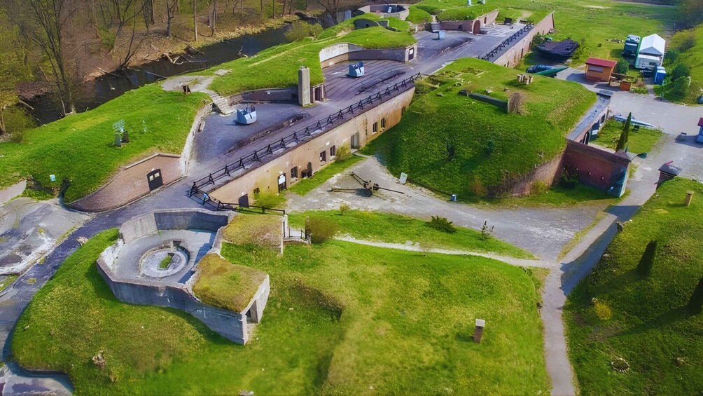 An aerial view of a historical fort with green roofs, a circular structure, and a river in the background. 4
