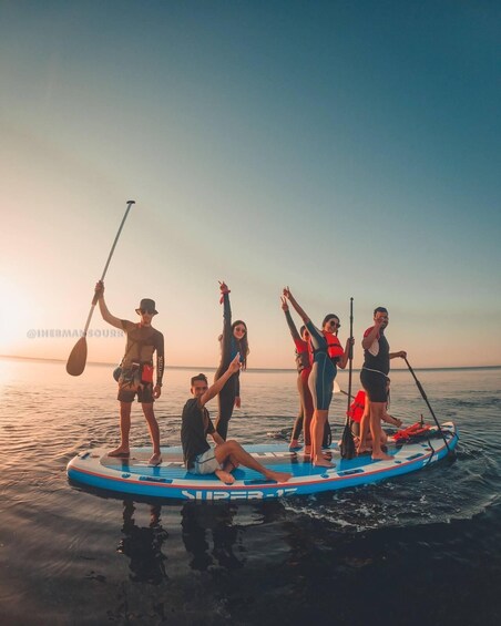 A group of people on a paddleboard at sunset. 2