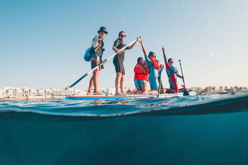 A group of people paddleboarding on a calm body of water with buildings in the background. 3