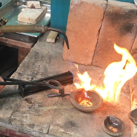 A traditional forge with a fire burning in a small metal container, surrounded by bricks and tools. 4